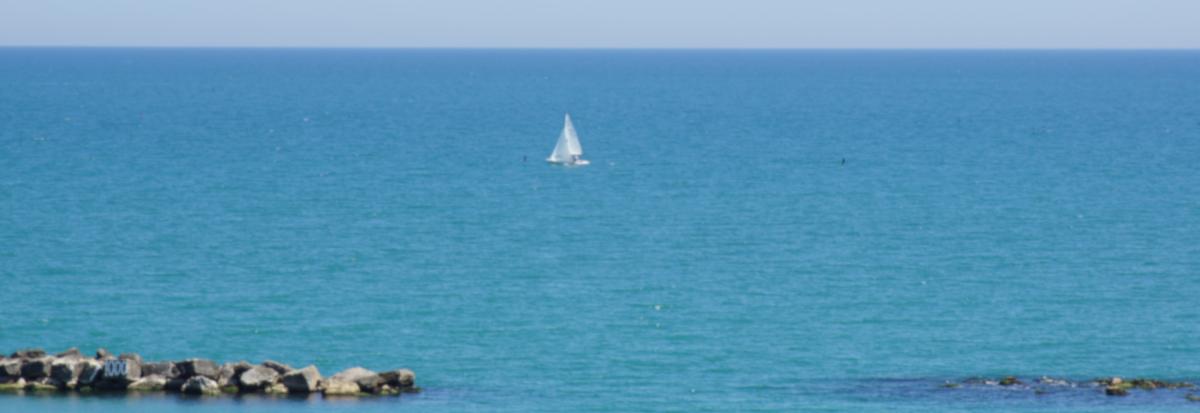 Ein Segelboot auf dem Meer, dahinter blauer Himmel.